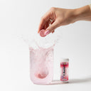 Hand dropping a pink tablet into a glass of water with a bottle labeled 'C-Buster' in the background.